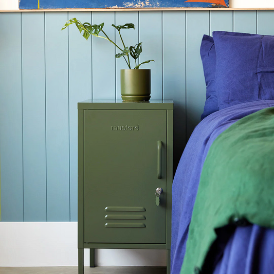 Green metal locker against a blue wall with a bed and plant in the foreground