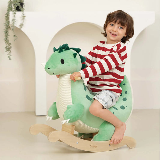 Child sitting on a green dinosaur-shaped rocking toy with a white background