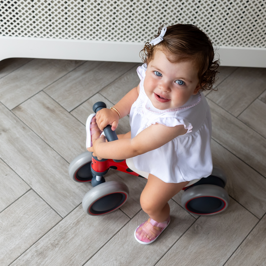 Child riding a red balance bike on a wooden floor.
