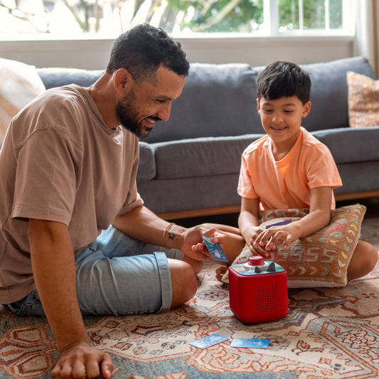 Man and child playing with a red toy on a patterned rug in a living room.