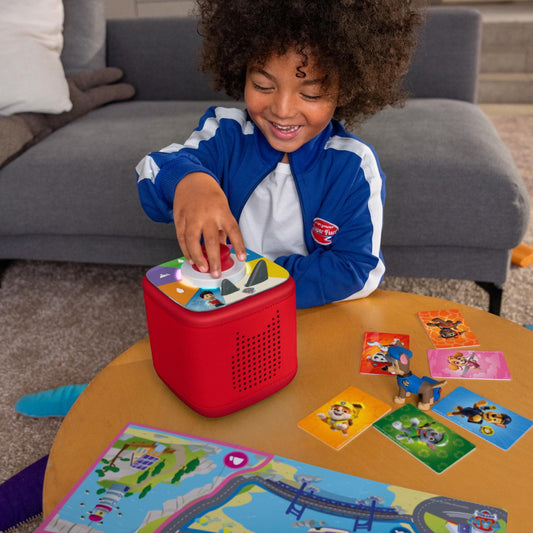 Child playing with a red toy on a table with colorful cards in a living room.