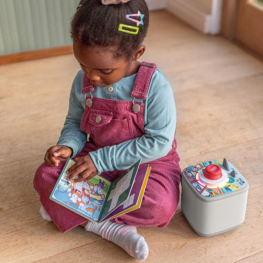 Child sitting on a wooden floor reading a book next to a toy box.
