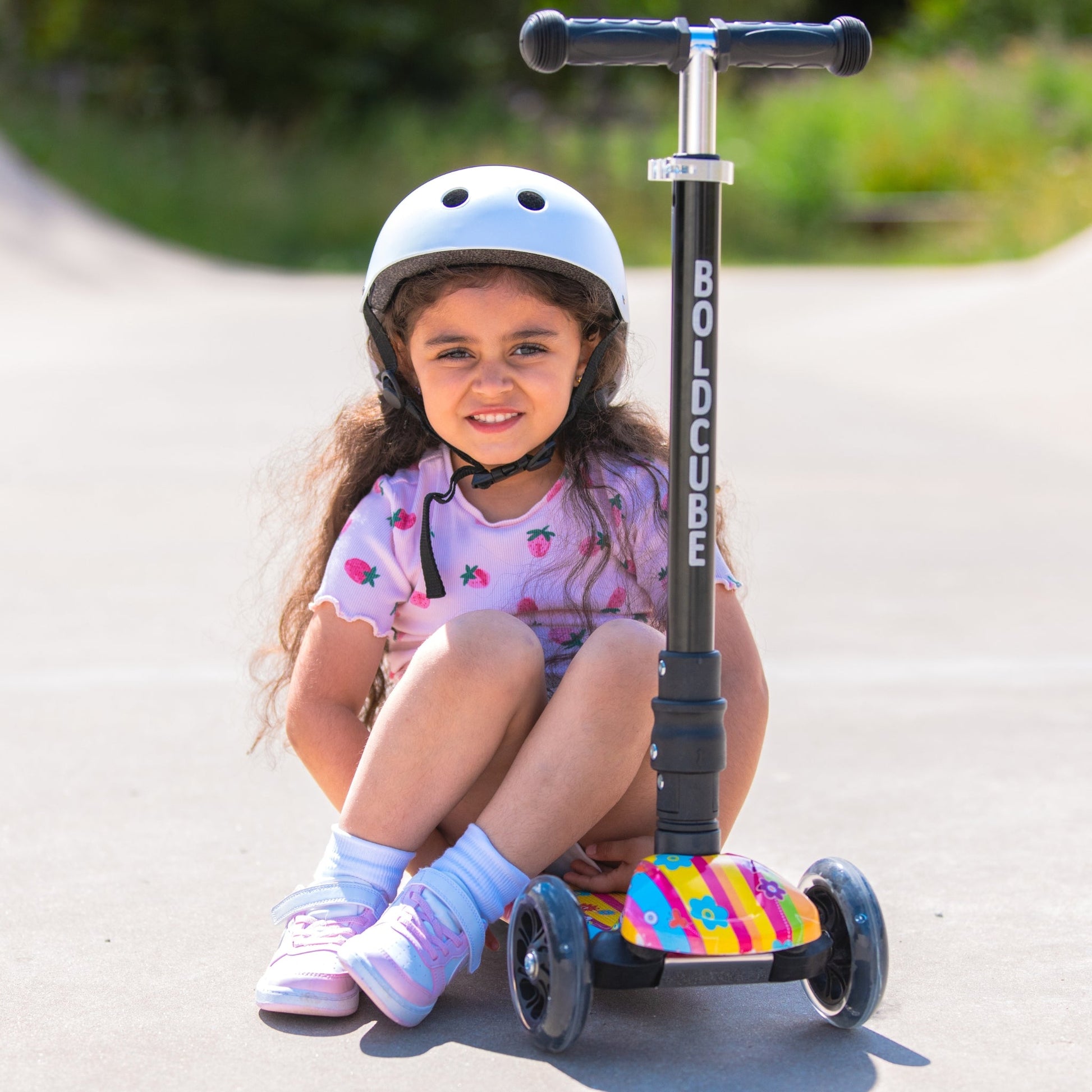 Child sitting on a colorful scooter with 'BaldCub' branding, wearing a helmet.