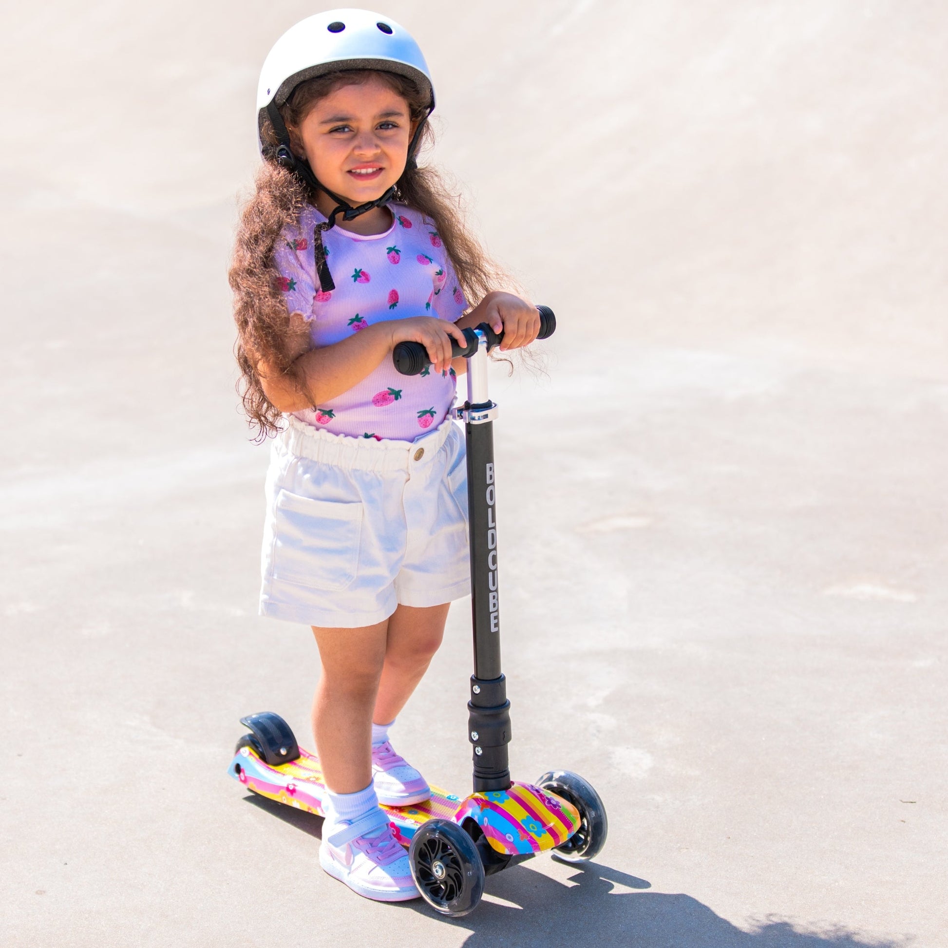 Child standing on a scooter wearing a helmet against a plain background