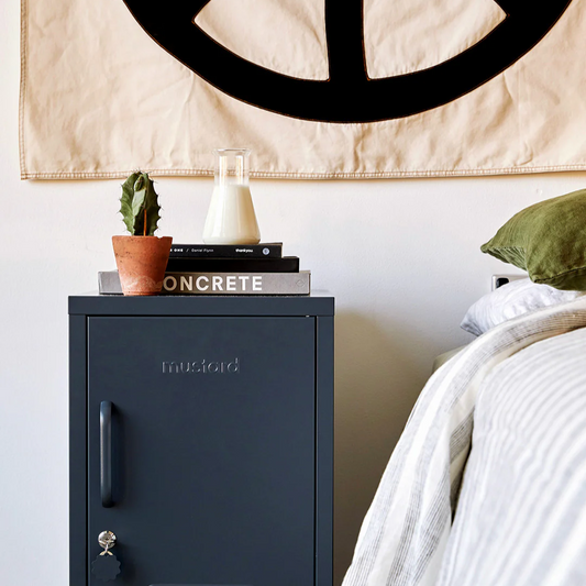 Peace symbol tapestry above a bed with a cabinet and books on a shelf.