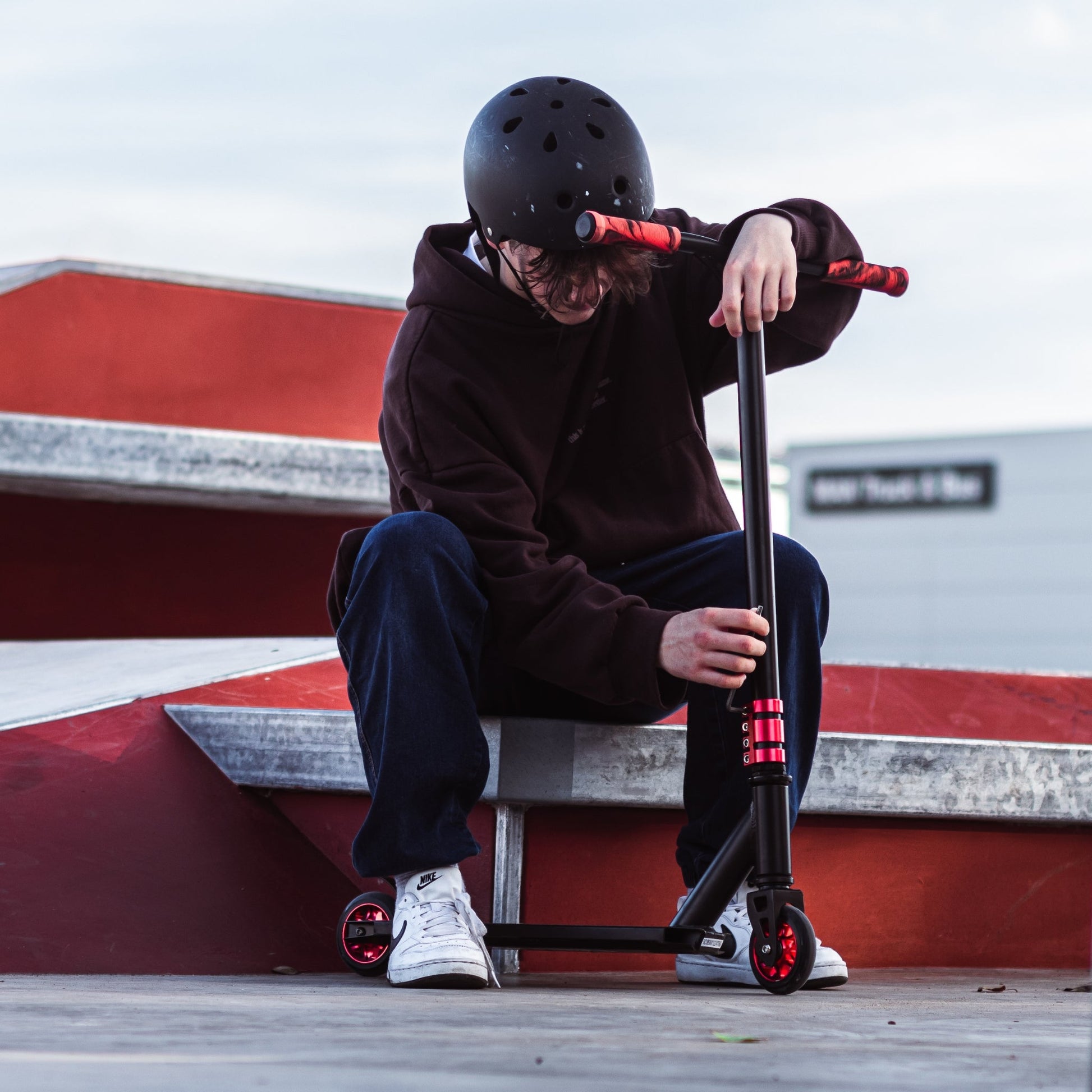 Person sitting on a red and white wall with a scooter, wearing a helmet.