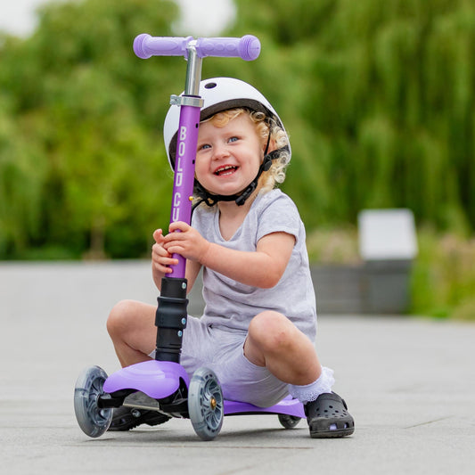 Child sitting on a purple scooter with a helmet outdoors