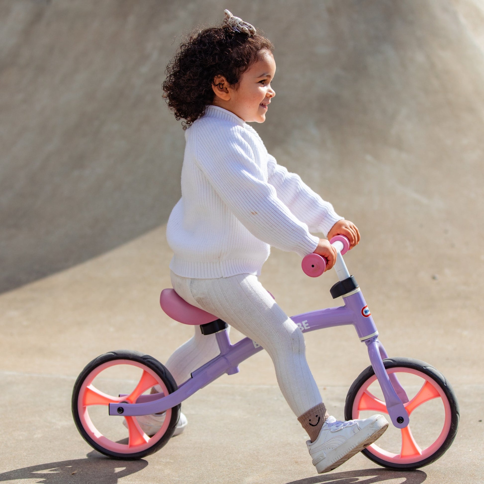 Child riding a pink balance bike on a concrete surface