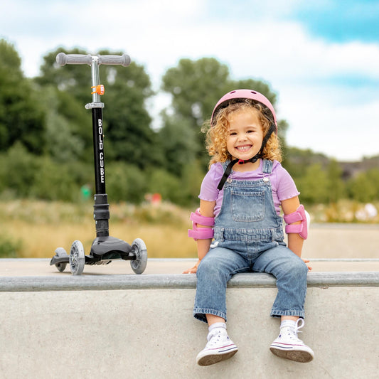Child sitting on a ledge with a scooter, wearing safety gear, in an outdoor setting.
