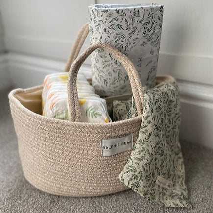 Woven basket with baby items including a blanket and diapers on a neutral background