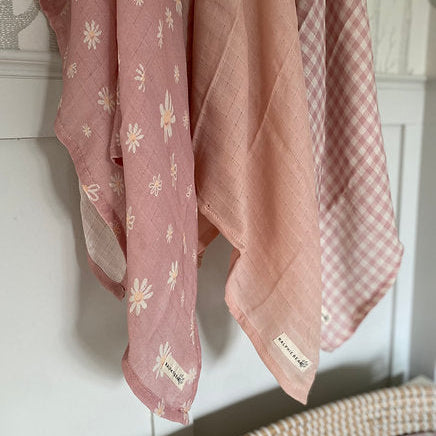 Pink fabric with floral and checkered patterns hanging on a white wall.