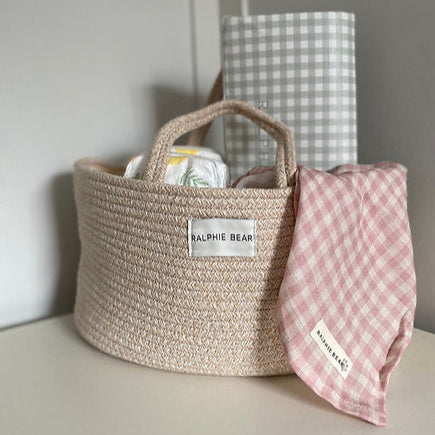 Woven basket with a checkered bag and pink checkered blanket on a neutral background