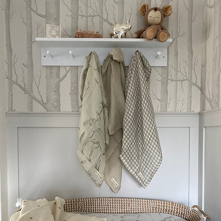 Nursery with baby blankets, toys, and a shelf against tree-patterned wallpaper.