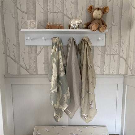 Nursery setup with changing table, towels, and teddy bear against a tree-patterned wall.