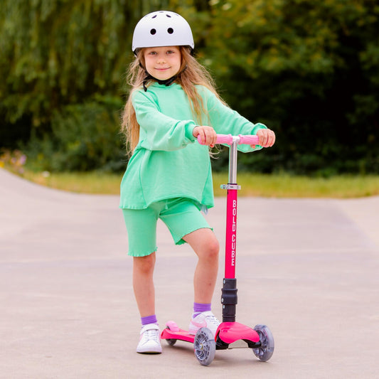 Child on a pink scooter wearing a helmet and green outfit outdoors.