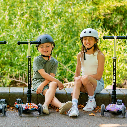 Two children sitting on a curb with their scooters, wearing helmets.