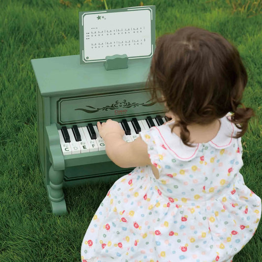 Child playing a green toy piano outdoors on grass
