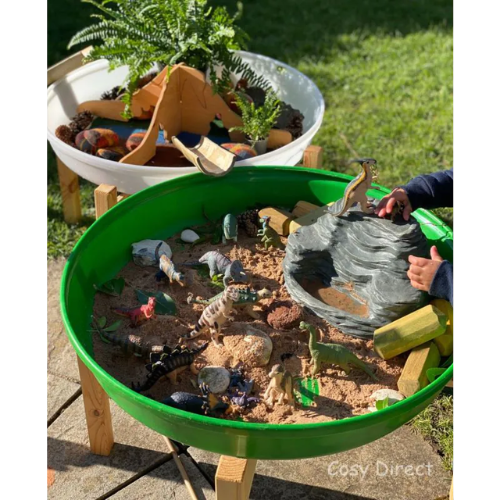 Children playing with toy dinosaurs and animals in a green sand pit outdoors.
