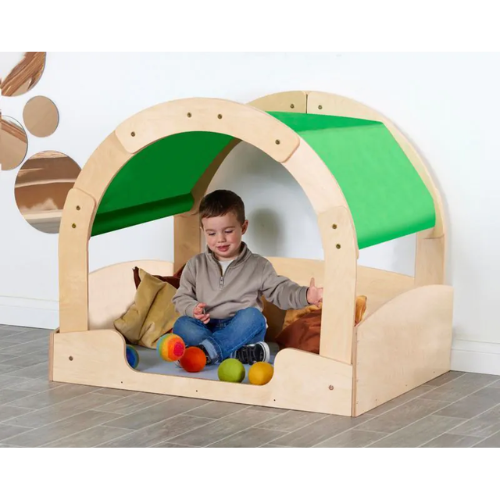 Child playing inside a wooden playhouse with a green roof on a tiled floor.