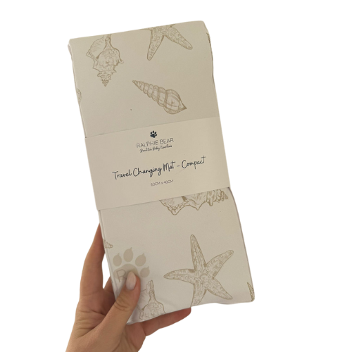 Folded travel changing mat with shell design held by a hand on a white background