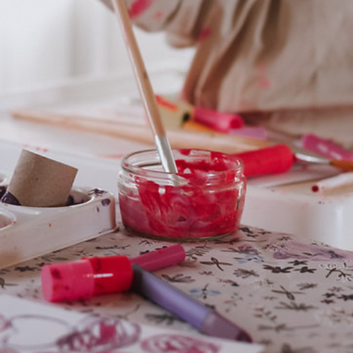 Person painting with red paint on a floral tablecloth