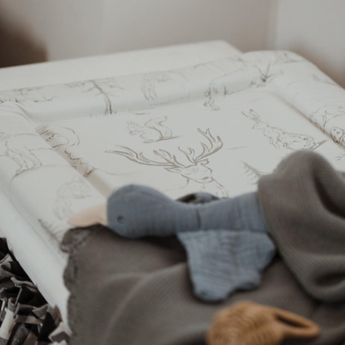 Baby crib with white mattress featuring deer patterns and a gray elephant toy.