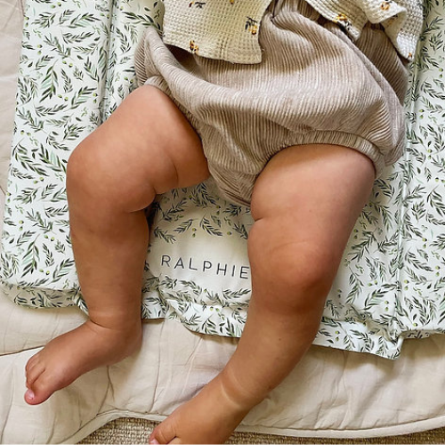 Baby legs wearing beige bloomers on a floral-patterned blanket with 'Ralphie' branding.