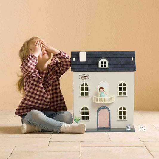 Child playing with a toy dollhouse on a wooden floor.