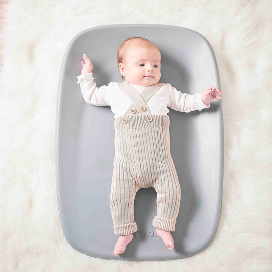 Baby lying on a gray mat with a white background