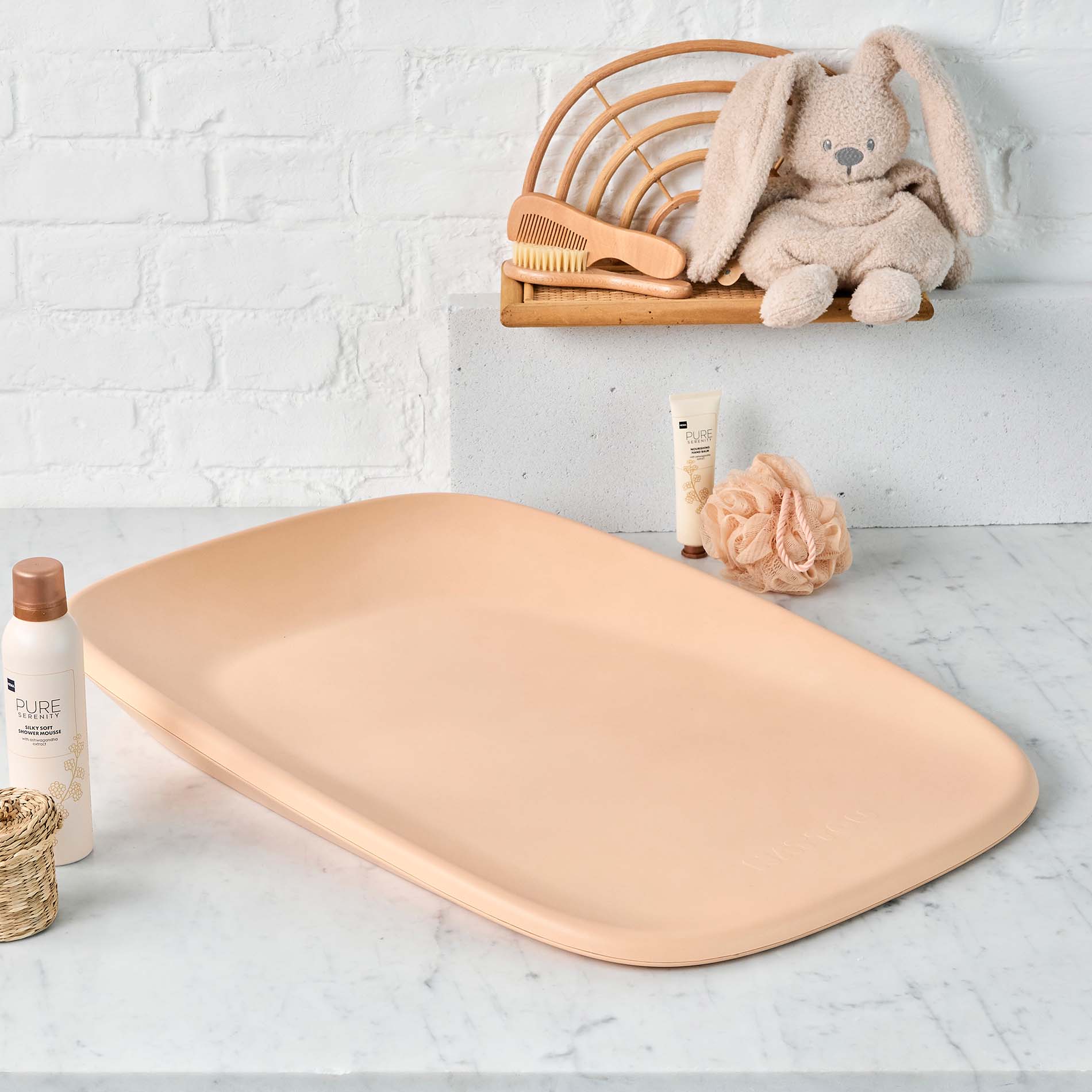Beige bath mat on a marble surface with baby products and a plush toy in the background.