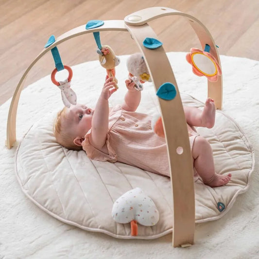 Baby playing with a wooden play gym on a soft surface