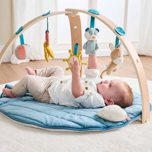 Baby playing with a wooden play gym on a blue mat
