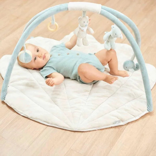 Baby lying on a white mat with a blue play gym