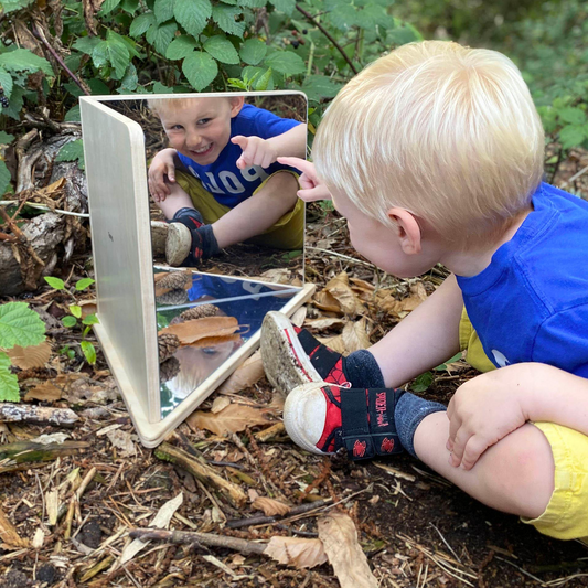 Child playing with a mirror outdoors, reflecting on nature.