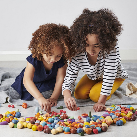 two children playing with loose parts on the floor.