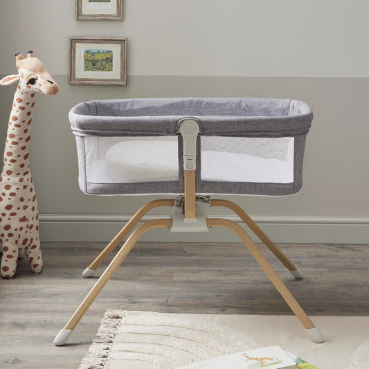 Portable crib on a stand in a room with a stuffed giraffe and framed pictures on the wall.