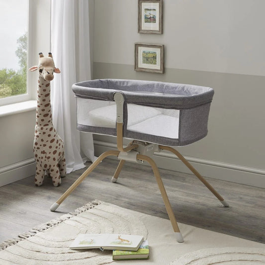 Gray baby crib with wooden legs in a room with a giraffe toy and books on a rug.