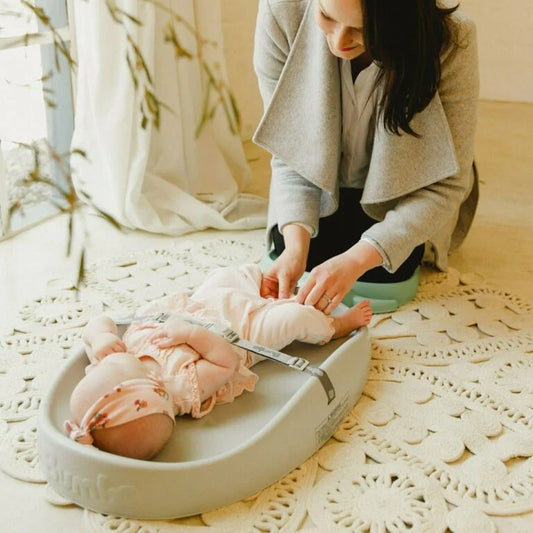 Woman adjusting a baby's diaper on a changing table with a neutral background