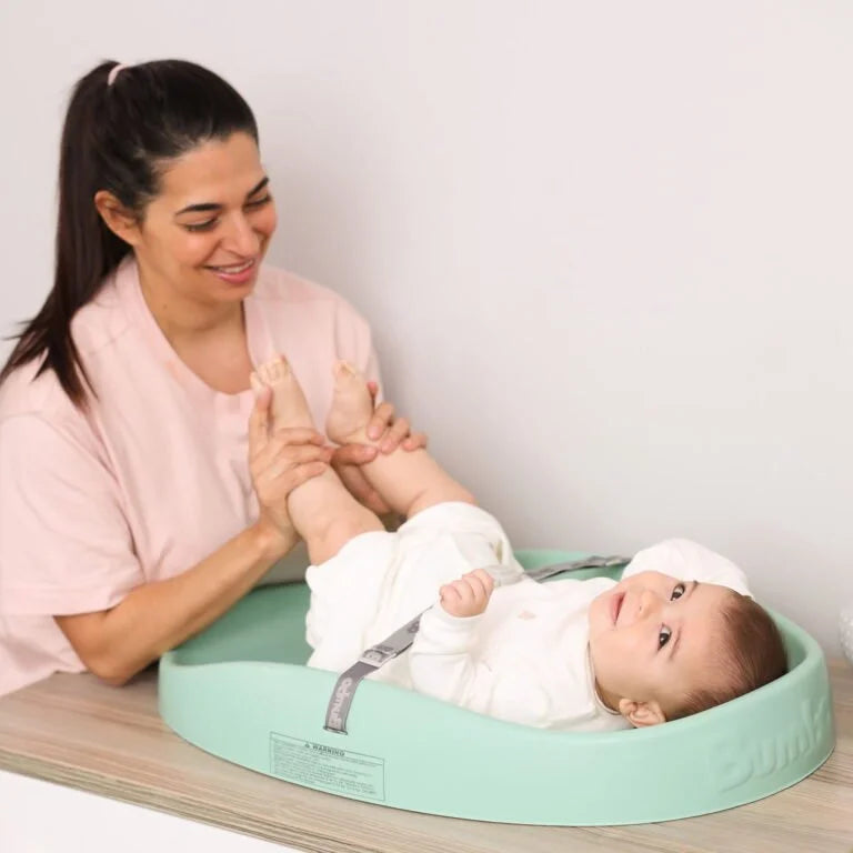 Woman interacting with a baby on a green baby seat against a white background