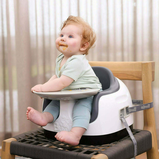 Baby sitting in a high chair with a tray, wearing a light green shirt and blue pants.