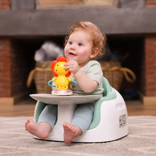 Baby sitting on a white and green stool holding a colorful toy in front of a fireplace.