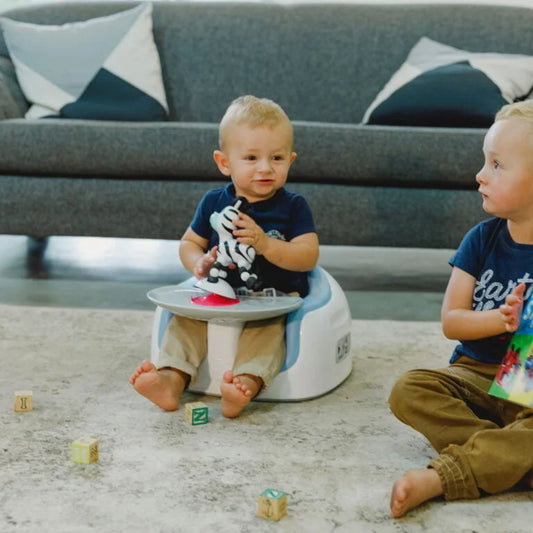 Two young children playing on a carpeted floor with toys and a potty chair.