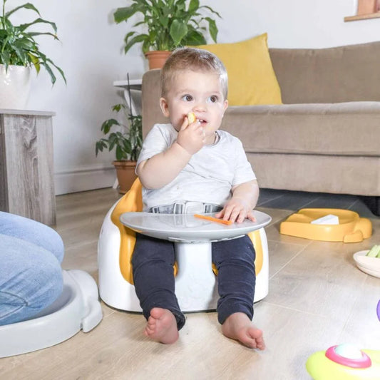 Child sitting on a white and yellow potty chair in a home setting with toys and plants around.