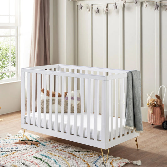 White crib in a nursery with a colorful rug and decorative elements.