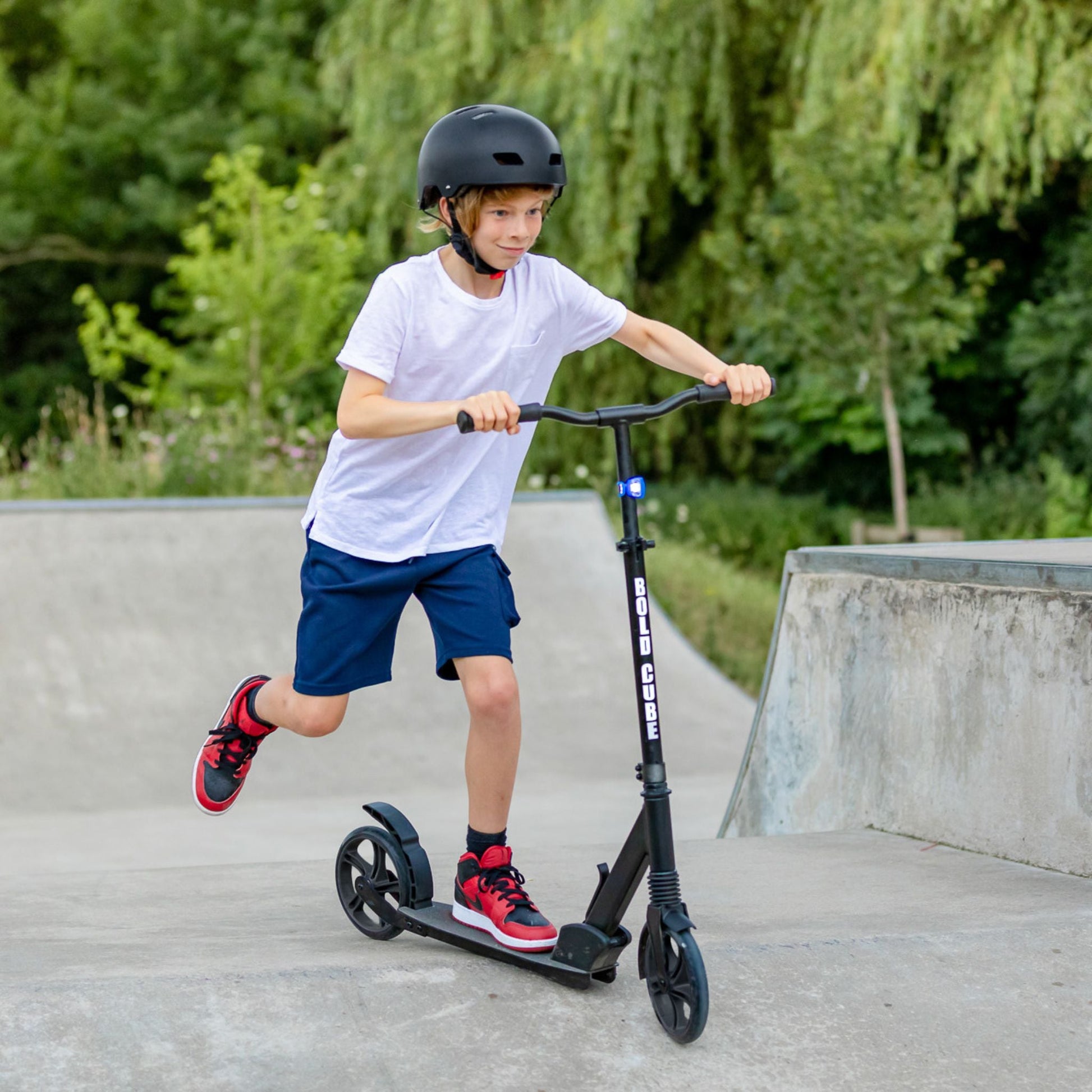 Child riding a scooter at a skate park with greenery in the background