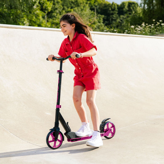 Girl in red outfit riding a scooter on a concrete surface with greenery in the background