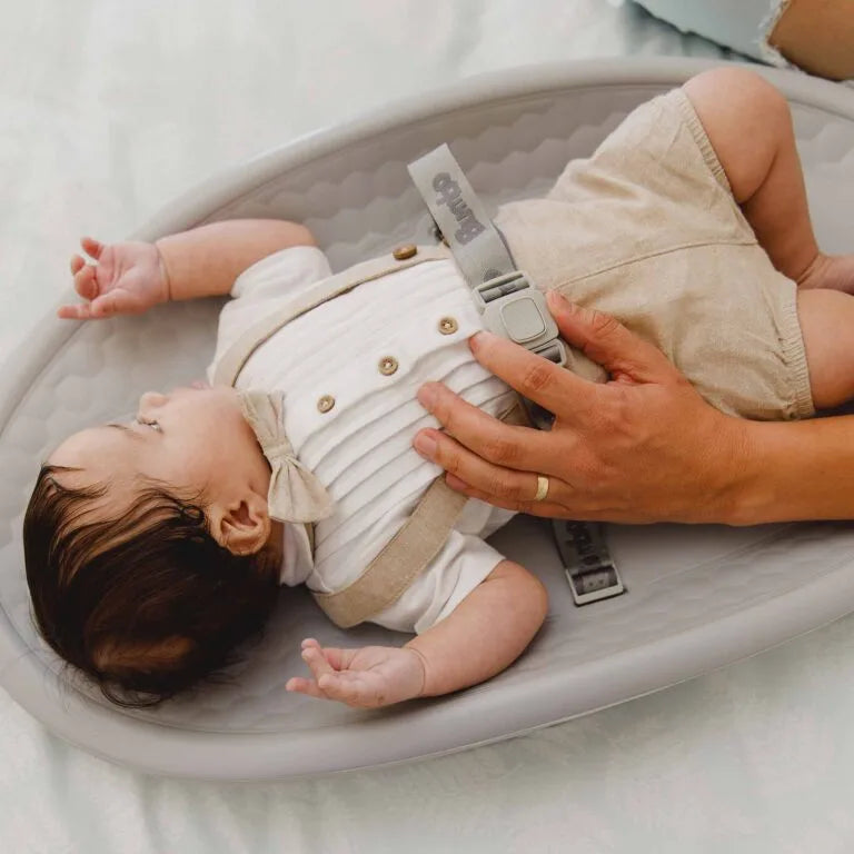 Baby lying on a gray bassinet with a person adjusting straps