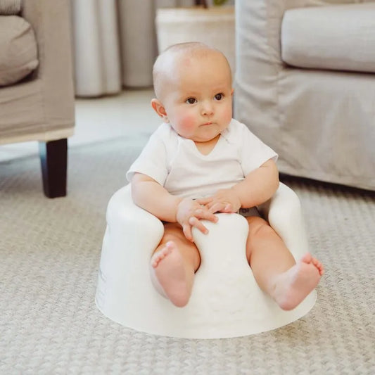 Baby sitting on a white cushioned stool in a living room.