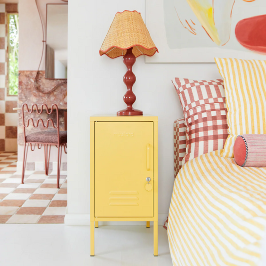 Yellow cabinet next to a bed with striped bedding and a lamp in a room.