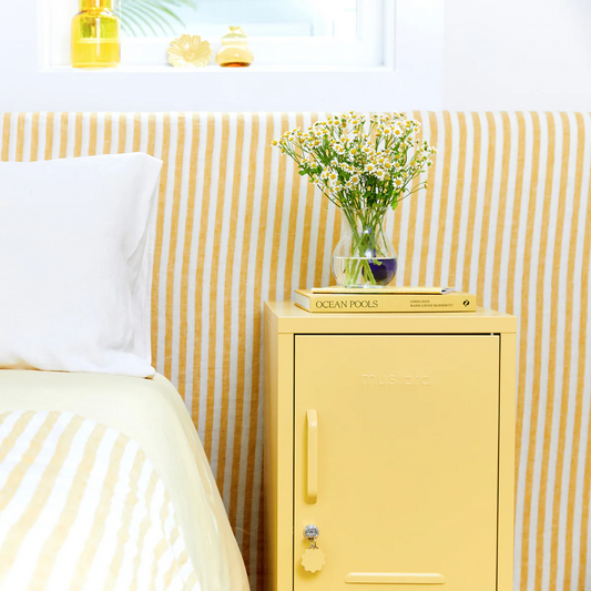 Yellow cabinet next to a bed with a striped headboard